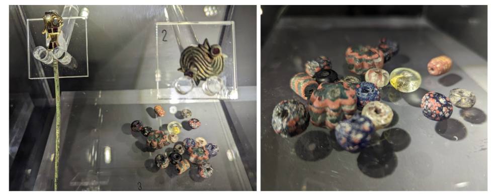 two photos show the beads and brooches excavated by ASE, displayed at Heritage Eastbourne. The beads are photographed close up – they are colourful an different shapes. The brooches are gold gilded and inset are pearls and garnets. Spotlights illuminate t