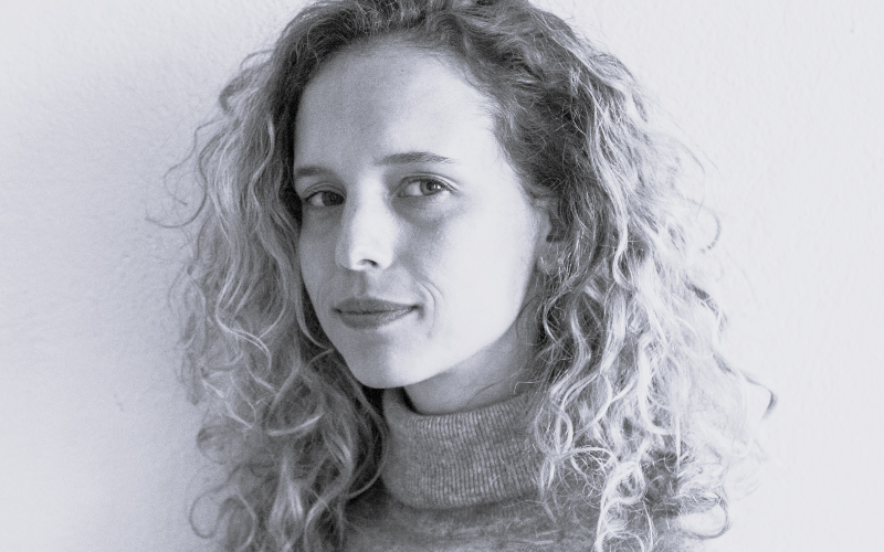 a young woman with curly hair and a grey top looks at the camera