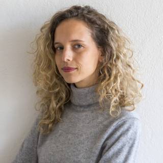 a young woman with curly blonde hair in a grey top looks at the camera