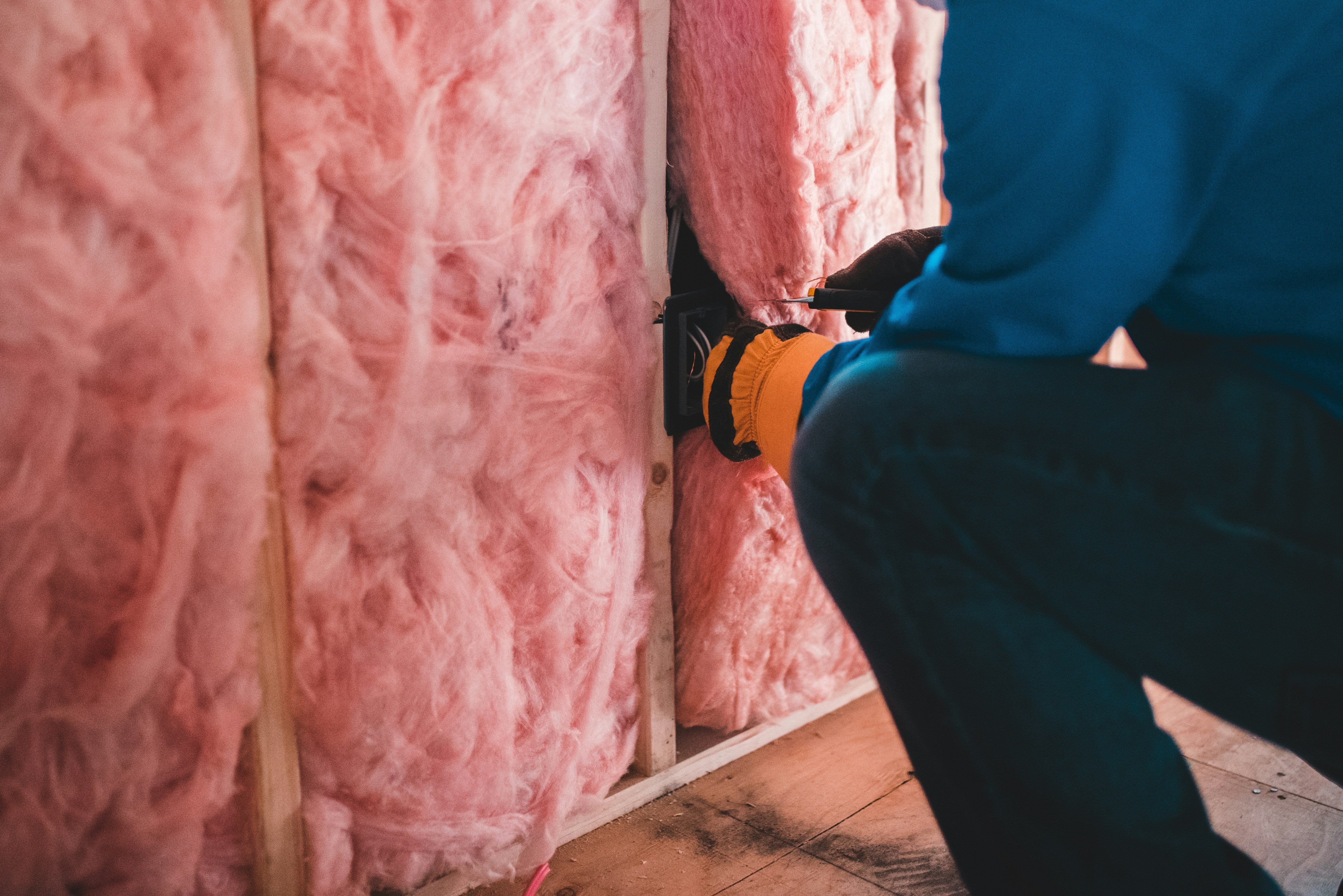 a gloved person installs insulation into a wall.