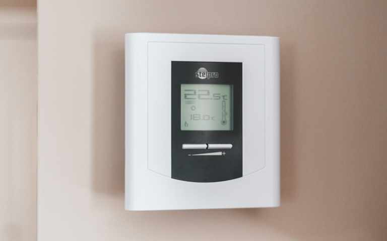 An electronic thermostat displaying the temperature at 18 celsius and the desired temperature as 22.5 celsius 