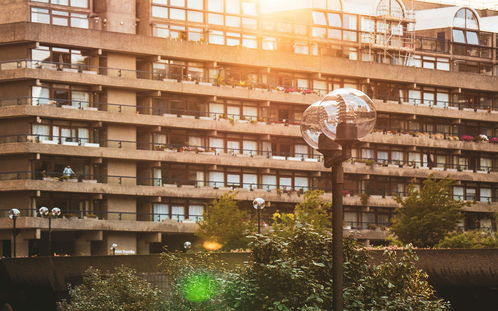 A lamppost in front of the terraces of the Barbican, London. The sunlight is coming from the top and as it's setting it's reflecting on the glass globe of the lamppost. 