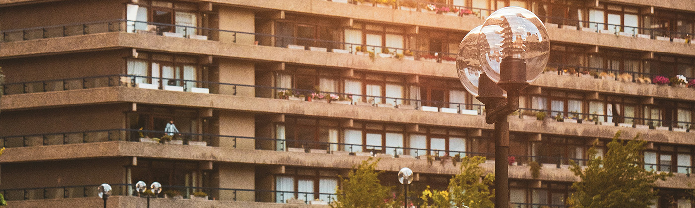 A lamppost in front of the terraces of the Barbican, London. The sunlight is coming from the top and as it's setting it's reflecting on the glass globe of the lamppost. 