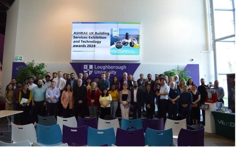 A group of people standing under a screen which reads 'ASHRAE UK Building Services Exhibition and Technology Awards 2024'