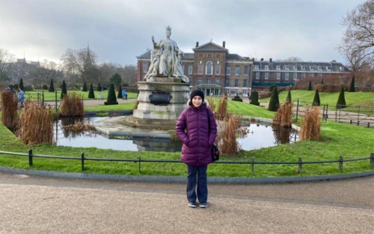 Nyma Haqqani stands in front an historic house wearing a purple puffa jacket and black beanie hat. Nyma is smiling but also looks cold.