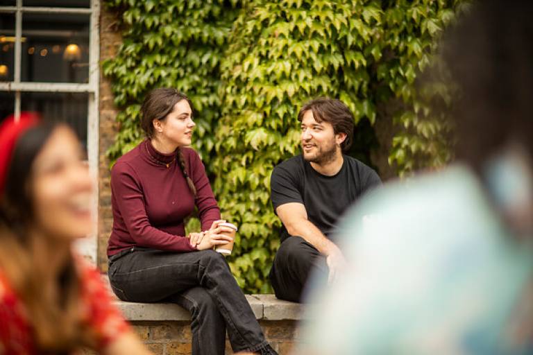 Students chat by an ivy covered wall