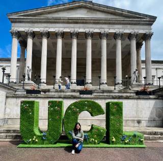Bidisha crouching in front of the UCL main building