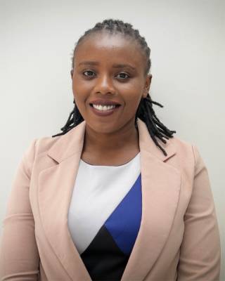 Maureen Muthike stands against a white background and is smiling at the camera while wearing a dusty pink suit jacket and braided hair. 