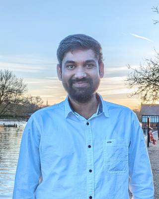 Viswanathan Veerappan stands in front of a lake smiling, wearing a blue shit at dusk