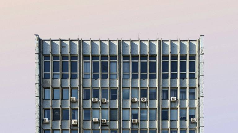 A high rise building in Chisinau, Moldova. There are many air conditioning units on it. It's against a sky that looks warm and muggy, shade of light grey, lilac and orange