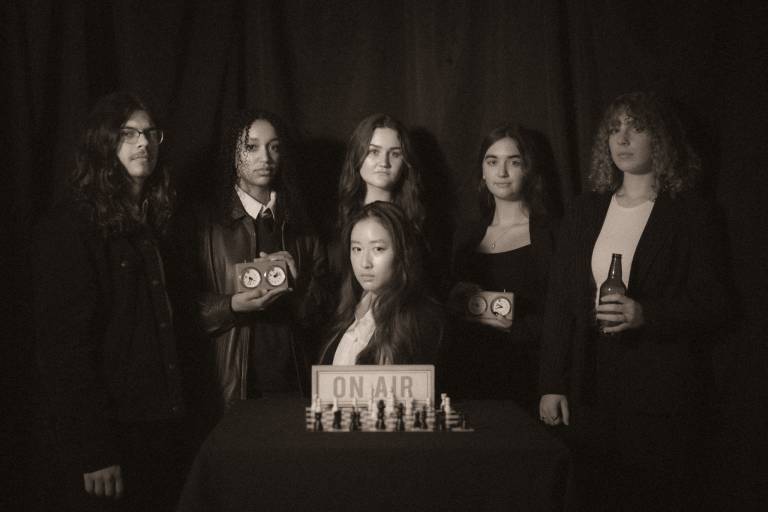 Black and white photo of the cast with chess set and timers