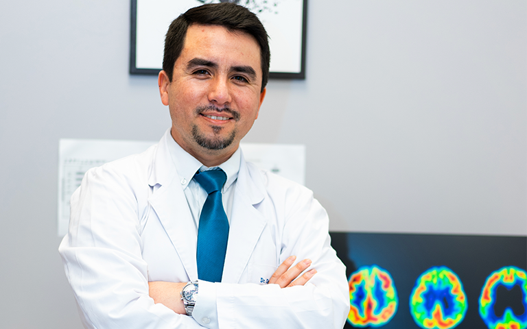 Dr Daniel Jimenez in a lab coat by a screen displaying brain cross sections