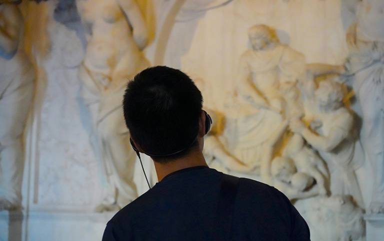 The back of a person's head with headphones on looking at a sculpture on the wall