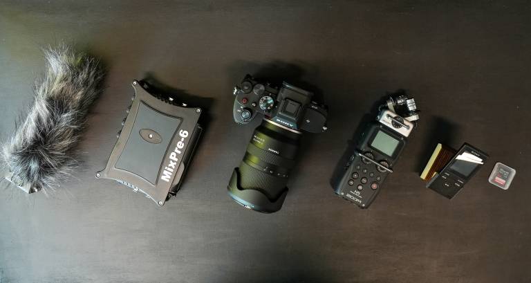 Row of high-spec technical equipment including SLR camera, audio recorder, microphone and memory cards