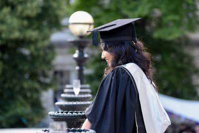 student in graduation cap and gown standing outside and smiling