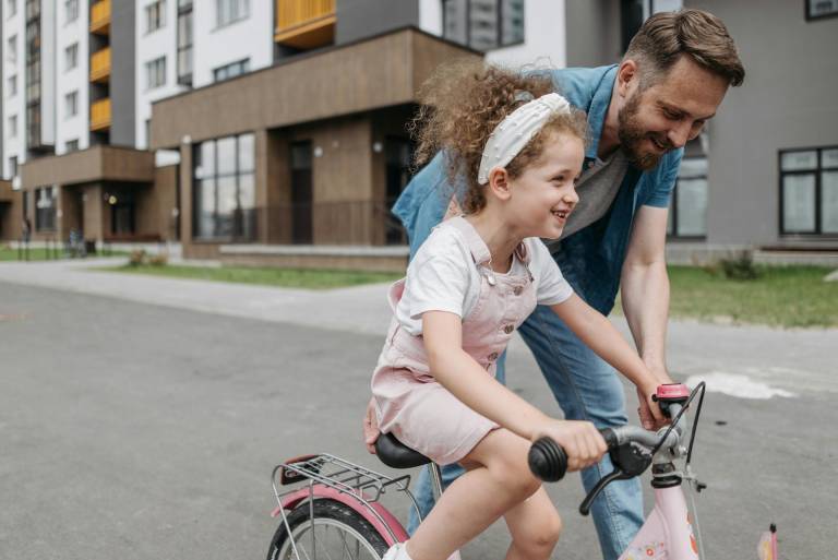 young girl riding bike with male guardian supporting her