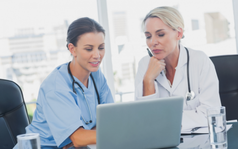 Two female doctors sit looking at a laptop