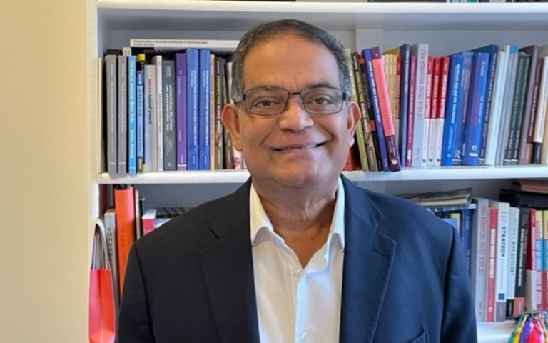 Amitav Acharya stands in an office, by some book shelves