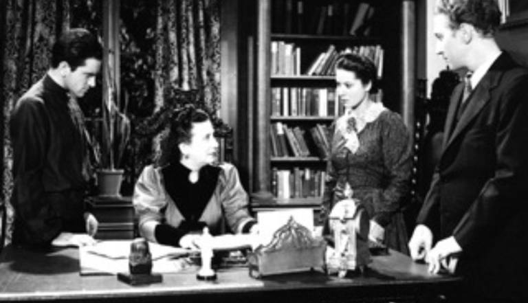 black and white photo of people gathered around a desk- probably a scene in the play