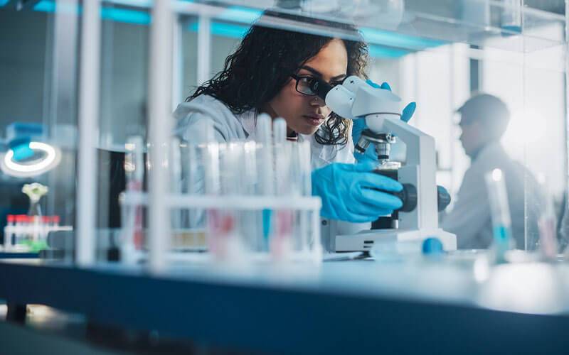 Lab researcher in white coat looking through a microscope