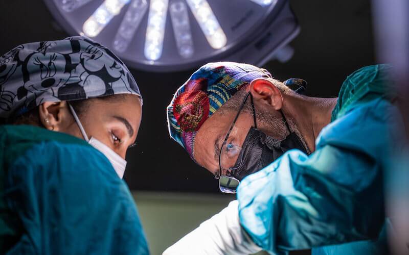 Two surgeons in protective equipment operating under surgical lights