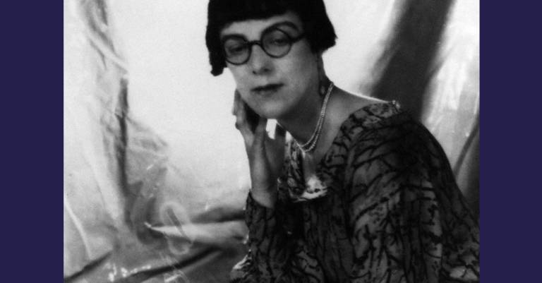 A detail of a black and white photograph of Sylvia Townsend Warner. Her gaze is fixing a point below the camera, she is wearing a pearl necklace, round glasses and has a short bob haircut