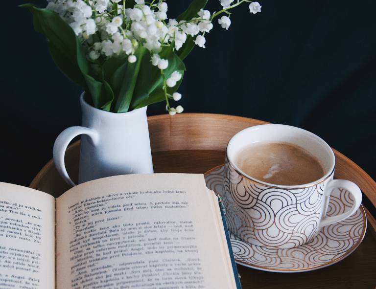 An open book next to a cup of coffee and a vase of snowdrops