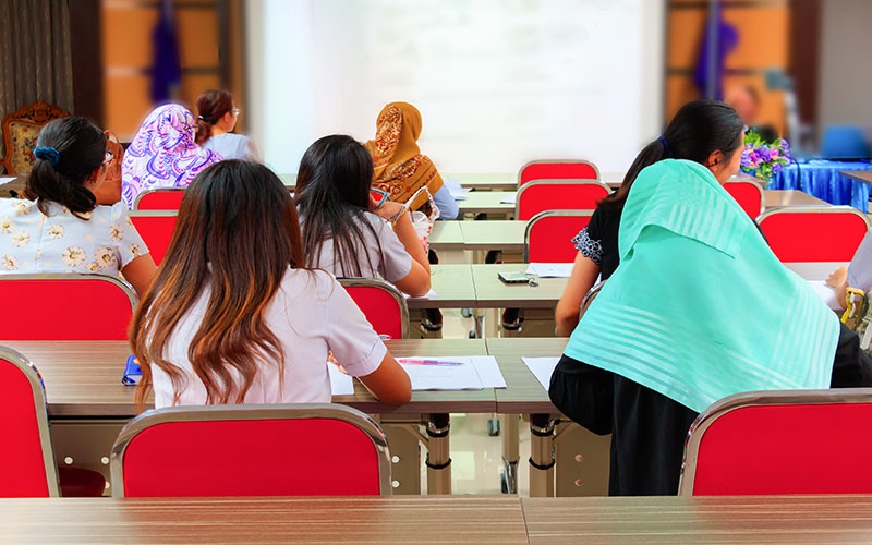 Back of students sitting on red chairs in classroom.