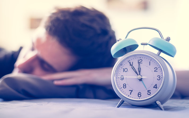 Alarm clock and a person sleeping in the background.