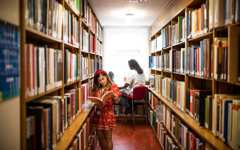  A student is looking at a book in between bookshelves in the library.