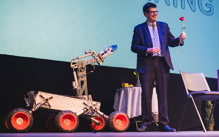 A person holding a flower in his hand with a rover next to him on a stage