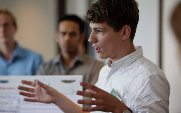 young man giving a presentation, in the background you can see people watching