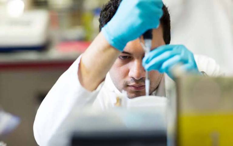 Scientist with gloves carefully manoeuvres a pipette