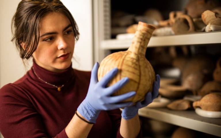 Person holding and examining a ceramic pot in the Petrie Museum