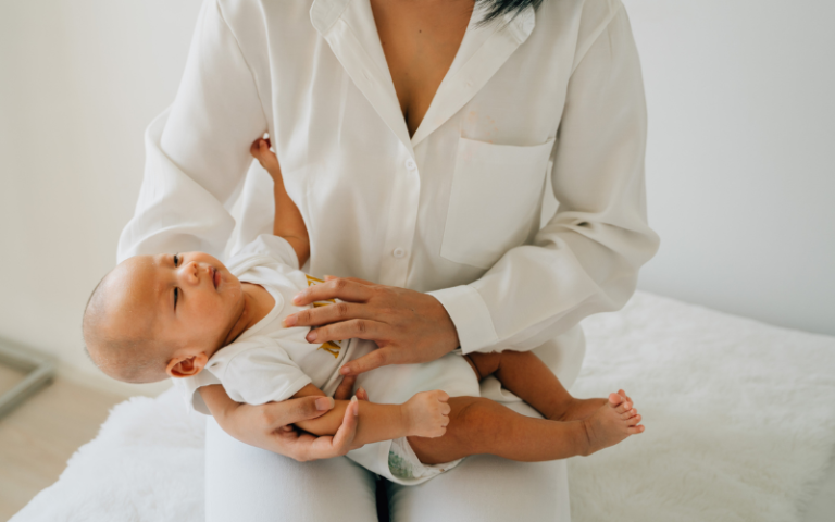 female in white wear holding own infant looking at little baby at home