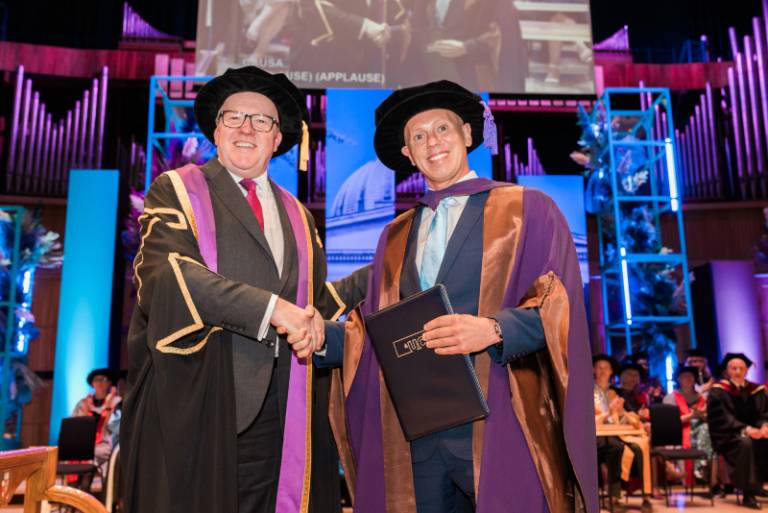 Professor Geraint Rees (left) shaking hands with Robert Rinder (right) at UCL's Graduation Ceremonies in May 2024. They are both wearing academic dress and smiling.