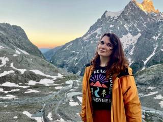 Alex Thompson standing in front of a mountain range with the sunset hitting lighting the peaks on the top right.