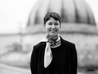 Monochrome headshot of Giovanna Tinett, standing in front of a domed building