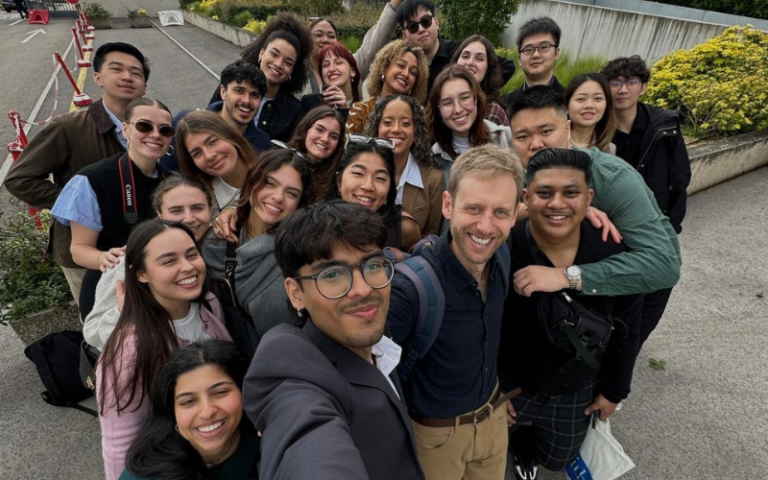 A group of smiling students take a selfie with their lecturer