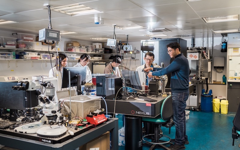 Five students in mechanical engineering lab housing multiple computers and technical equipment on tables