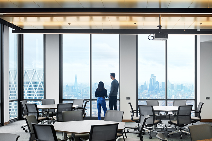 Two people in open plan office looking out of window of skyscraper