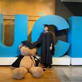 Student Zekun Wu standing in front of large UCL letters in blue next to a large teddy bear