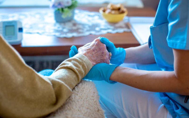 nurse with gloves on holding an elderly lady's hand