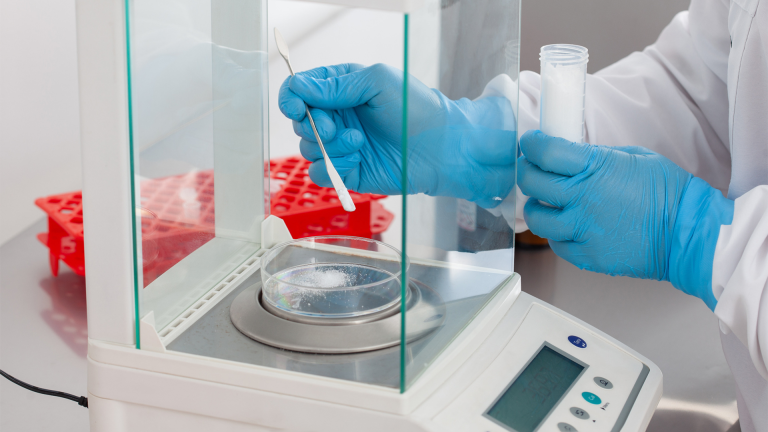 Person wearing safety gloves hand weighing a chemical on scales