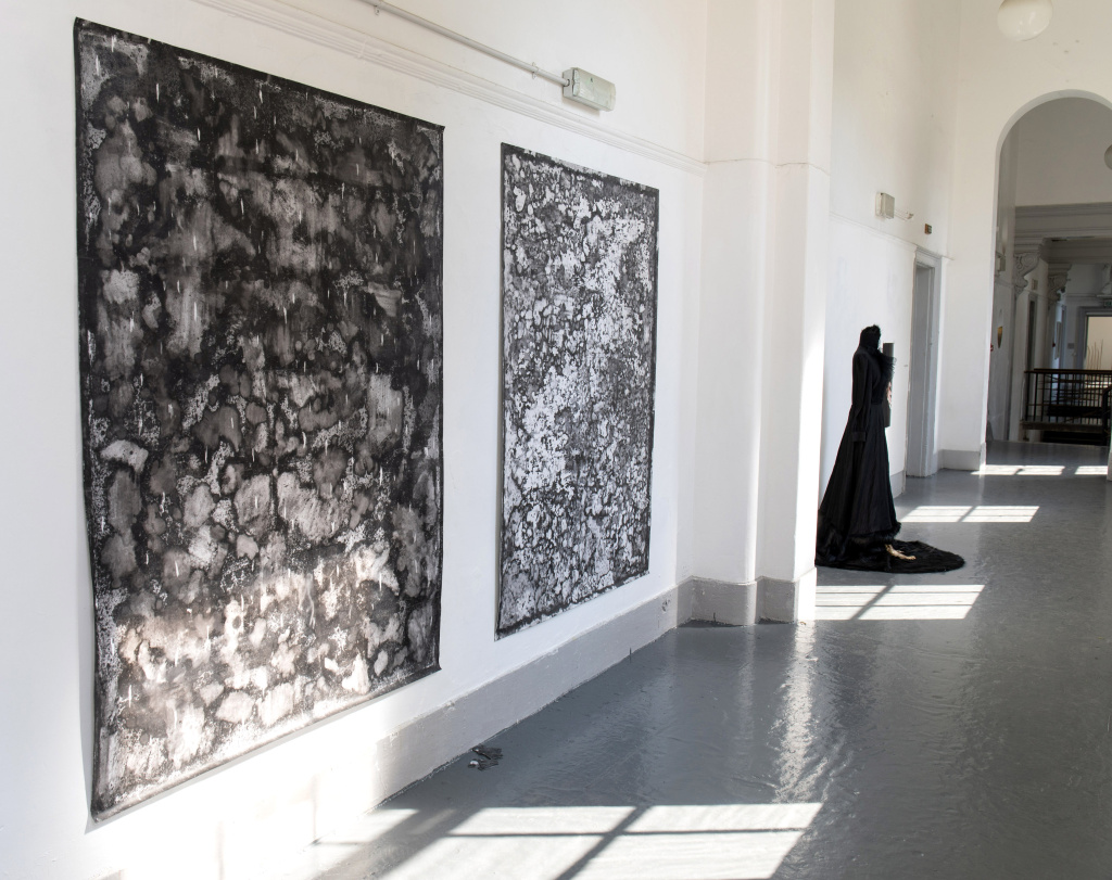 Installation photo, foreground two abstract greyscale paintings by Camilo Parra and behind figurative sculpture in long black dress by  Kasia Garapich/Katarzyna Depta-Garapich