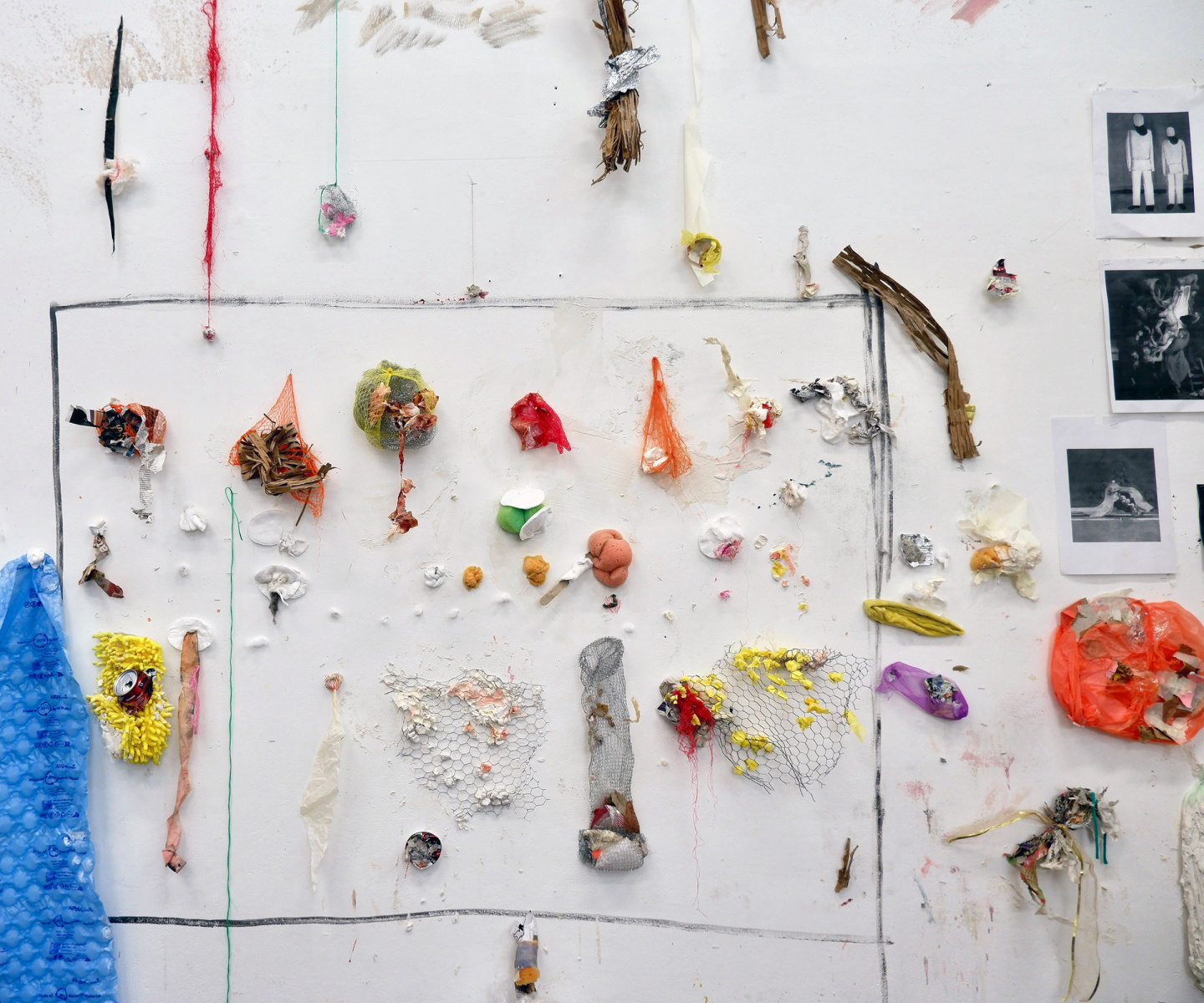 Studio wall with scraps paintings: fruit netting, cotton wool, sponges, scourer, chicken wire, newspaper, masking tape, paper packaging, hairband, can, string, tissue paper, white tack, adhesive plaster, towel, wooden fork.
