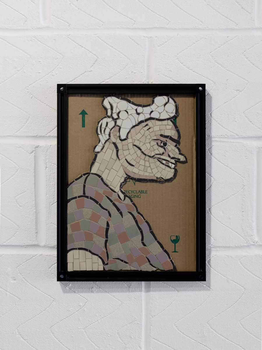 A grotesque mosaic caricature of a person in profile. The person is smiling, and the mosaic is in the style of 1800 satirical cartoons. It is stuck to an old cardboard panel from a box used for shipping. The assembly is housed in an aluminium v-slot frame.