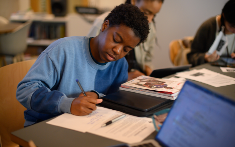 Image shows a student writing notes on a desk