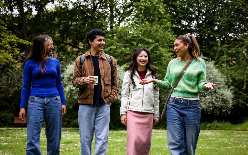 Image shows four students walking across a park and smiling 