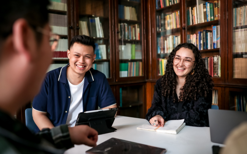 Image shows two students smiling against a backdrop of books 